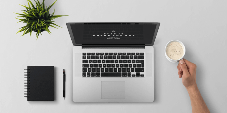 Someone sitting in front of a laptop with a cup of coffee in hand.